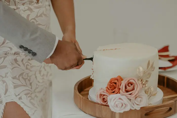 A white wedding cake with blush roses being cut
