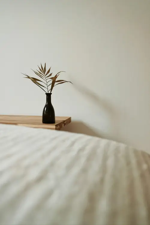 A vase with a dried leaf on a bedside table